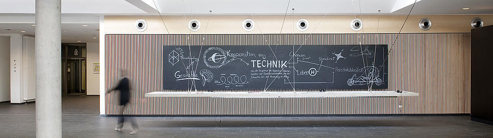 A slate with inscriptions hangs in the foyer of a modern building.
