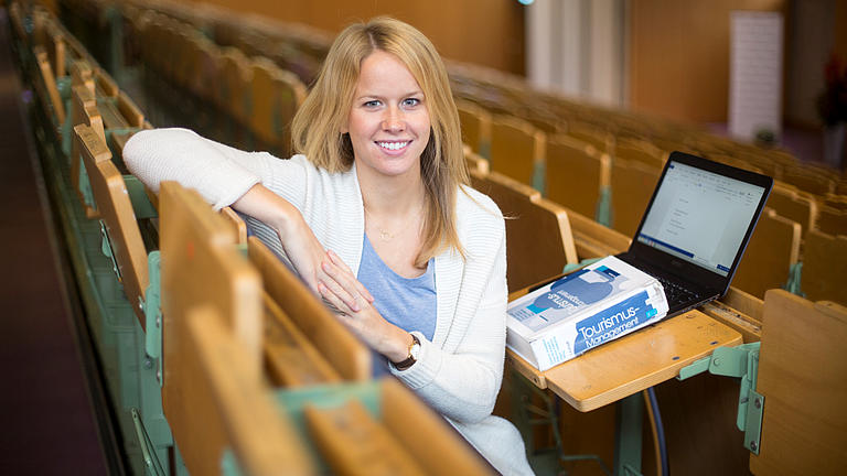 Studentin sitzt mit Laptop und Buch in einem Hörsaal.