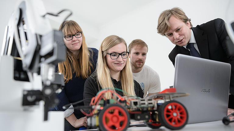 Studierende am Laptop beim Auswerten eines Experimentes im Vordergrund steht ein Modellauto aus Lego