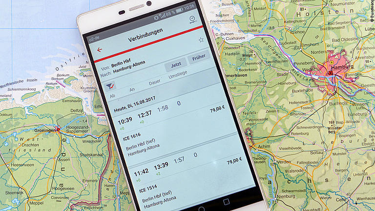 Ein Smartphone liegt auf einer Karte Nordwestdeutschlands. Auf dem Display ist eine Reisenavigationsapp geöffnet.