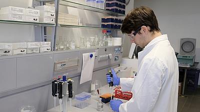 Ein junger Mann im Laborkittel füllt im Labor mit einer Pipette eine Flüssigkeit in ein Glas.