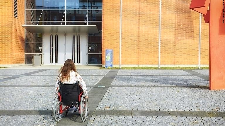 Eine Studentin im Rollstuhl bewegt sich auf dem Campus einer Hochschule.