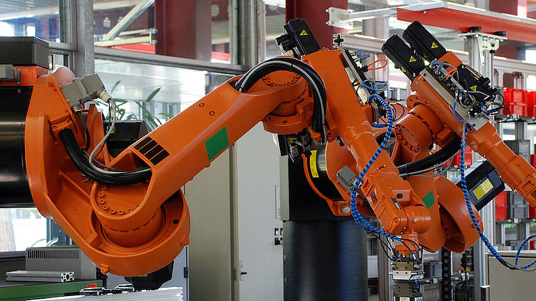 Ein großer oranger Roboterarm steht in einer Werkhalle