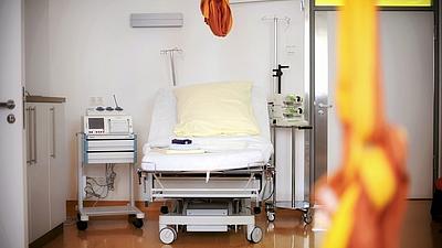 Blick in einen Kreißsaal. Neben dem Entbindungsbett stehen verschiedene medizinische Geräte. Von der Decke hängt ein Tuch.