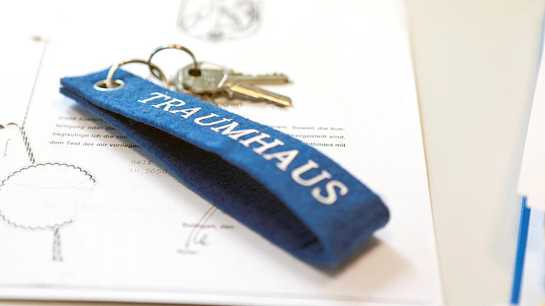 Auf einem notariellen Schriftstück liegt ein Schlüssel mit einem blauen Schlüsselanhänger aus Filz mit der Aufschrift Traumhaus.