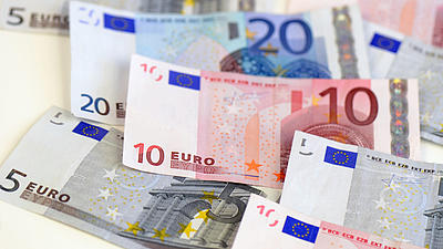 Auf einer hellen Oberfläche liegen verschiedene Geldscheine in Euro-Währung.