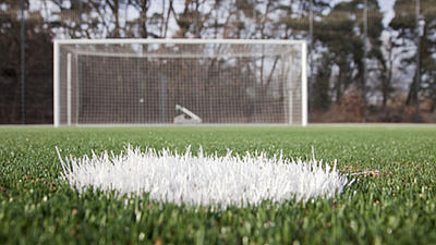 Fußballrasen mit einer Ballmarkierung und einem Fußballtor, aufgenommen vom Abstoßpunkt sehr weit unten über dem Rasen.