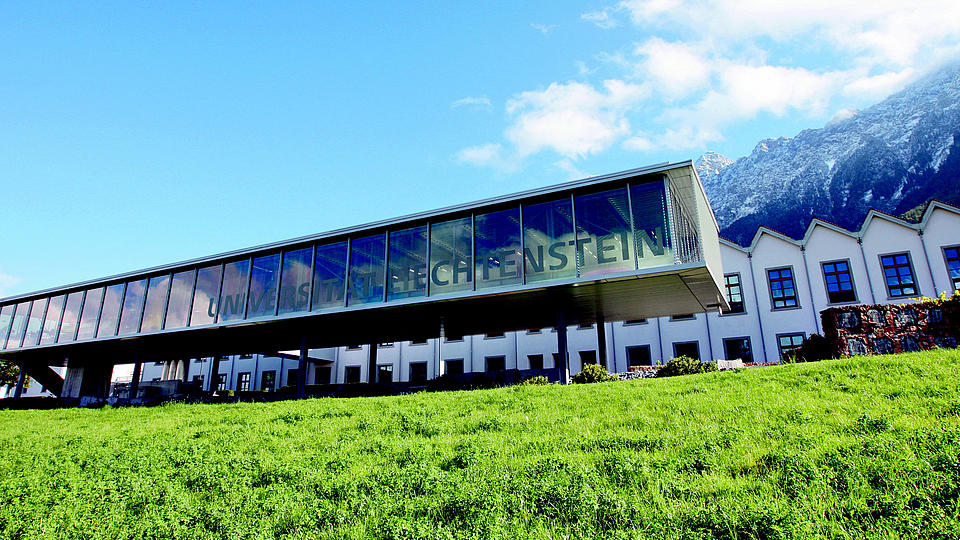 Außenansicht der Universität Liechtentein mit Bergen im Hintergrund blauem Himmel und grünem Gras im Vordergrund