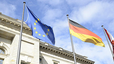 Die Europaflagge und die Deutschlandfahne wehen vor einem Gebäude.