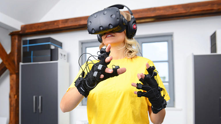 Eine Frau trägt eine Virtual-Reality-Brille und Fingerhandschuhen mit Sensoren.