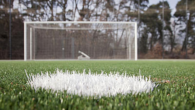 Fußballrasen mit einer Ballmarkierung und einem Fußballtor, aufgenommen vom Abstoßpunkt sehr weit unten über dem Rasen.