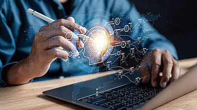 Person am Laptop aktiviert mit einem elektronischen Stift holografische Symbole über der Tastatur. 