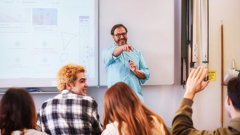 Der Lehrer ruft einen Schüler auf, der sich meldet.