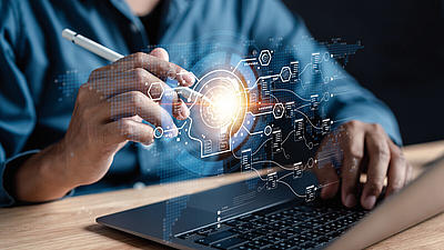 Person am Laptop aktiviert mit einem elektronischen Stift holografische Symbole über der Tastatur.