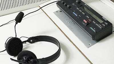 Auf einer weißen Oberfläche steht ein Dolmetscher-Mikrofon und Kopfhörer mit Mundstück liegen daneben.
