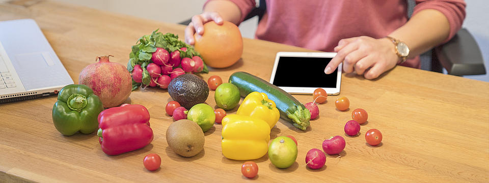 Verschiedene Gemüsesorten liegen auf einem Tisch, dahinter ein Man mit einem Tablet