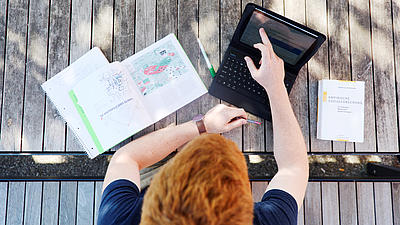 Ein Studierender sitzt mit Laptop auf einer Bank.