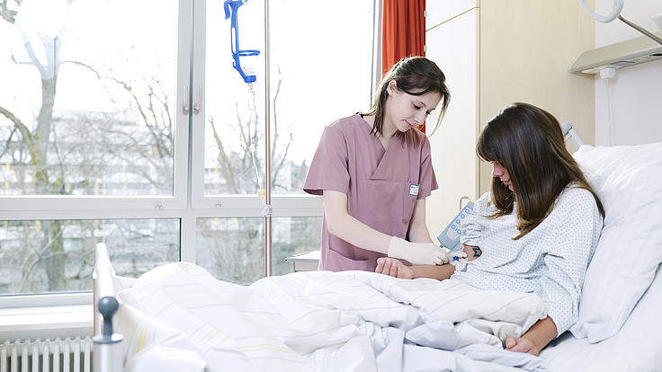Junge Krankenpflegerin bereitet eine Patientin für eine Infusion vor.