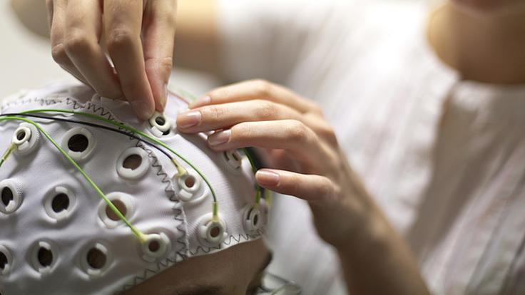 Nahaufnahme einer Frau die an einer Haube, die von einer Person getragen wird, Elektroden anschließt, um eine Hirnstrommessung durchzuführen.